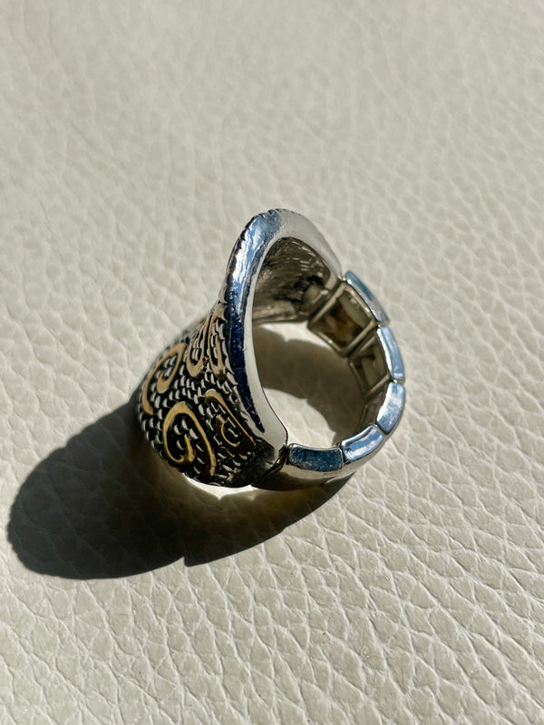 Silver ring with intricate designs on a light beige textured surface