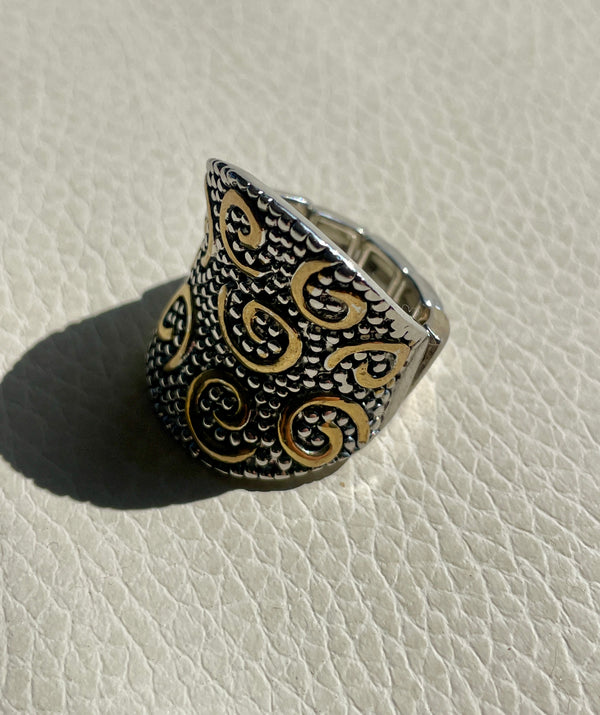 Silver ring with intricate gold patterns on a light gray surface