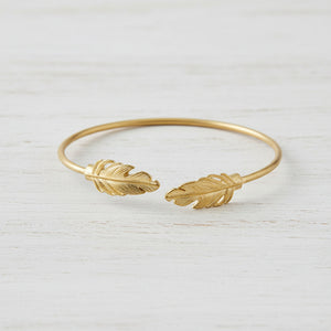 Gold bracelet with feather designs on a white background