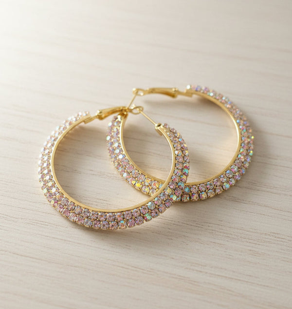 Gold hoop earrings with gemstones on a light wooden surface