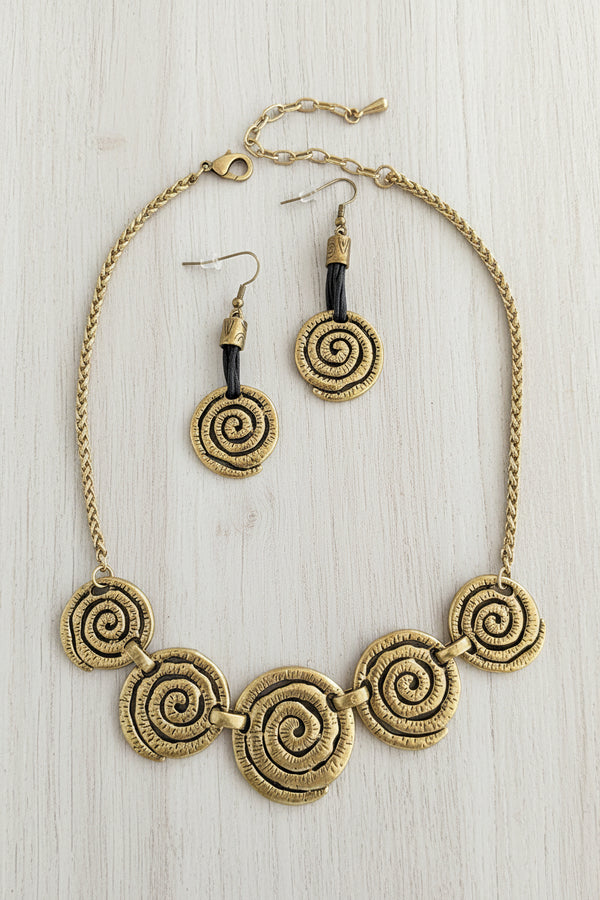 Gold spiral necklace and earrings on a dark textured surface