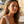 Load image into Gallery viewer, Woman with earrings standing in front of a scenic background with buildings and palm trees.
