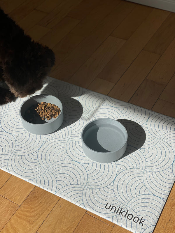 Pet bowls on a patterned mat with 'uniklook' branding on a wooden floor.