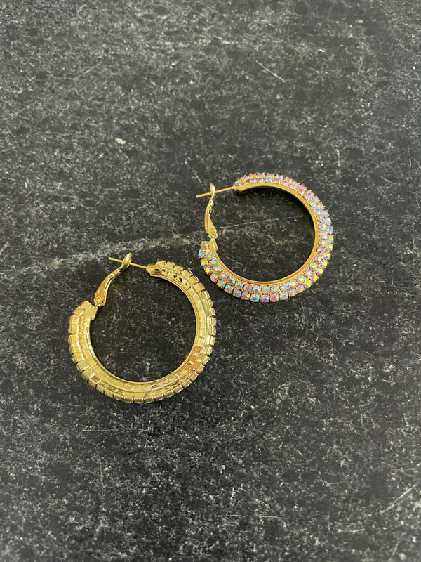 Gold hoop earrings with embedded stones on a dark textured surface