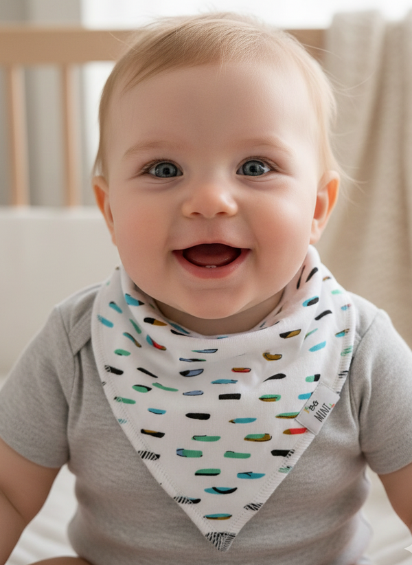 Baby wearing a colorful bib sitting in a crib