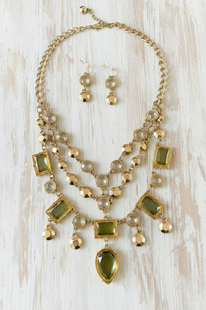 Necklace and earrings set with green and clear stones on a dark surface