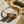 Load image into Gallery viewer, Gold bracelet with black stones on a stone surface with sand and driftwood in the background
