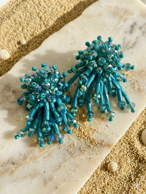 Turquoise beaded earrings on a textured surface with sand-like material