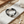 Load image into Gallery viewer, Black leather bracelet with white beads on a marble surface with sand and stones.
