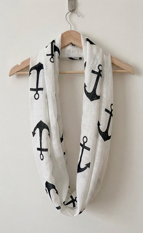 White infinity scarf with black anchor patterns draped over a wooden hanger on a white background.
