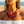 Load image into Gallery viewer, A close-up lifestyle shot of a woman on a beach wearing a chunky statement necklace. The necklace features large, layered translucent red disc elements woven with red beads and accented with small silver beads.
