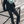 Load image into Gallery viewer, Person wearing a black sweater, green scarf, and black pants on a city street.
