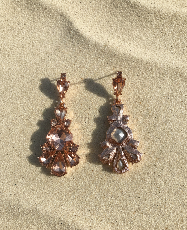 Pair of ornate earrings on a sandy surface