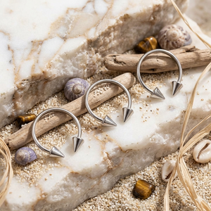 Silver hoop earrings with spike details on a natural stone surface with shells and driftwood.