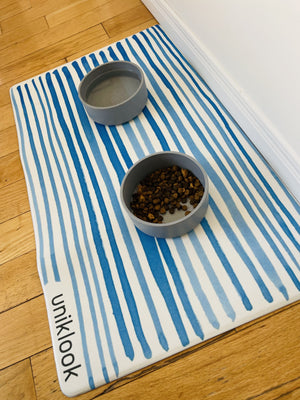 Striped mat with two gray bowls on a wooden floor, featuring the brand 'uniklook'.