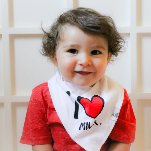 A baby wearing a red shirt and a white bandana bib with the text 'I love milk' printed on it.